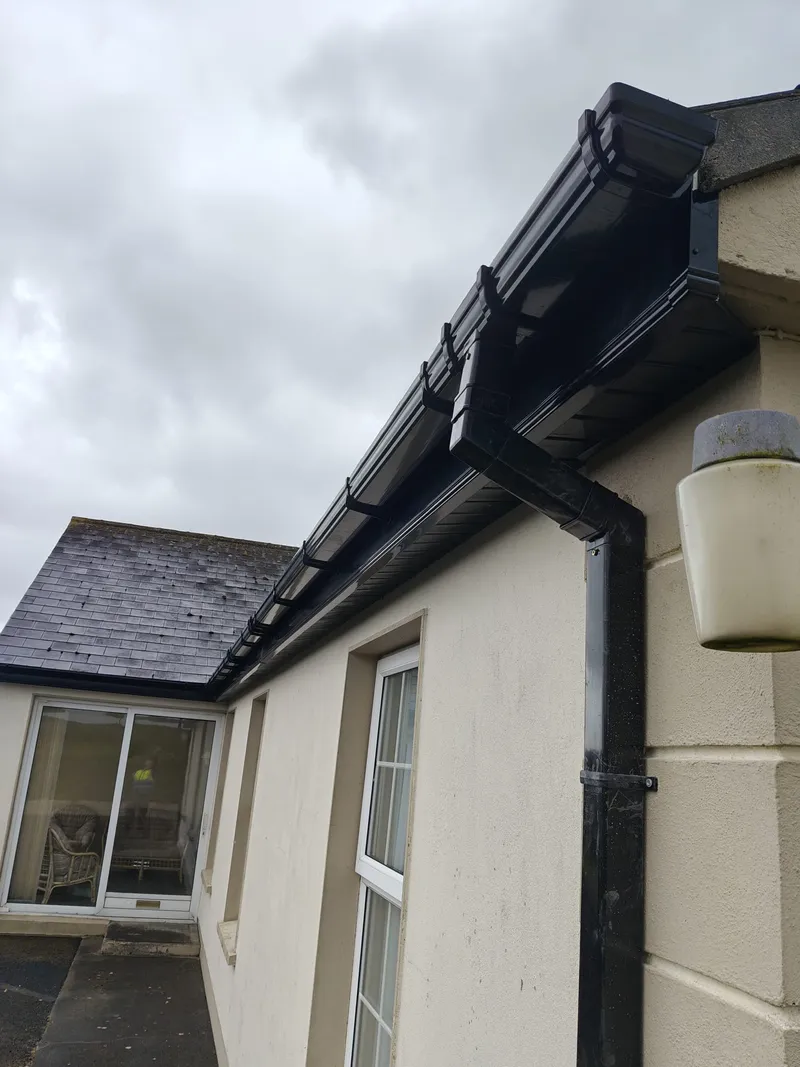 Black half-round gutter, fascia and downpipe at the eaves of a house with a slate roof