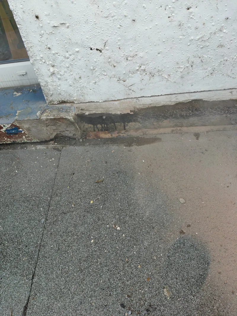 Flat roof surface with staining and a worn edge where the felt meets a painted wall