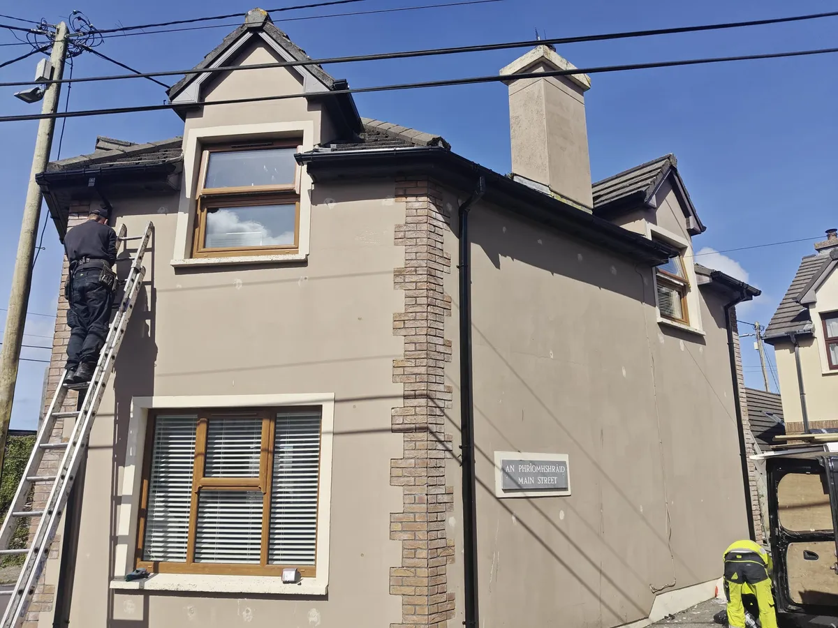 A roofer on a ladder at the eaves of a two-storey house