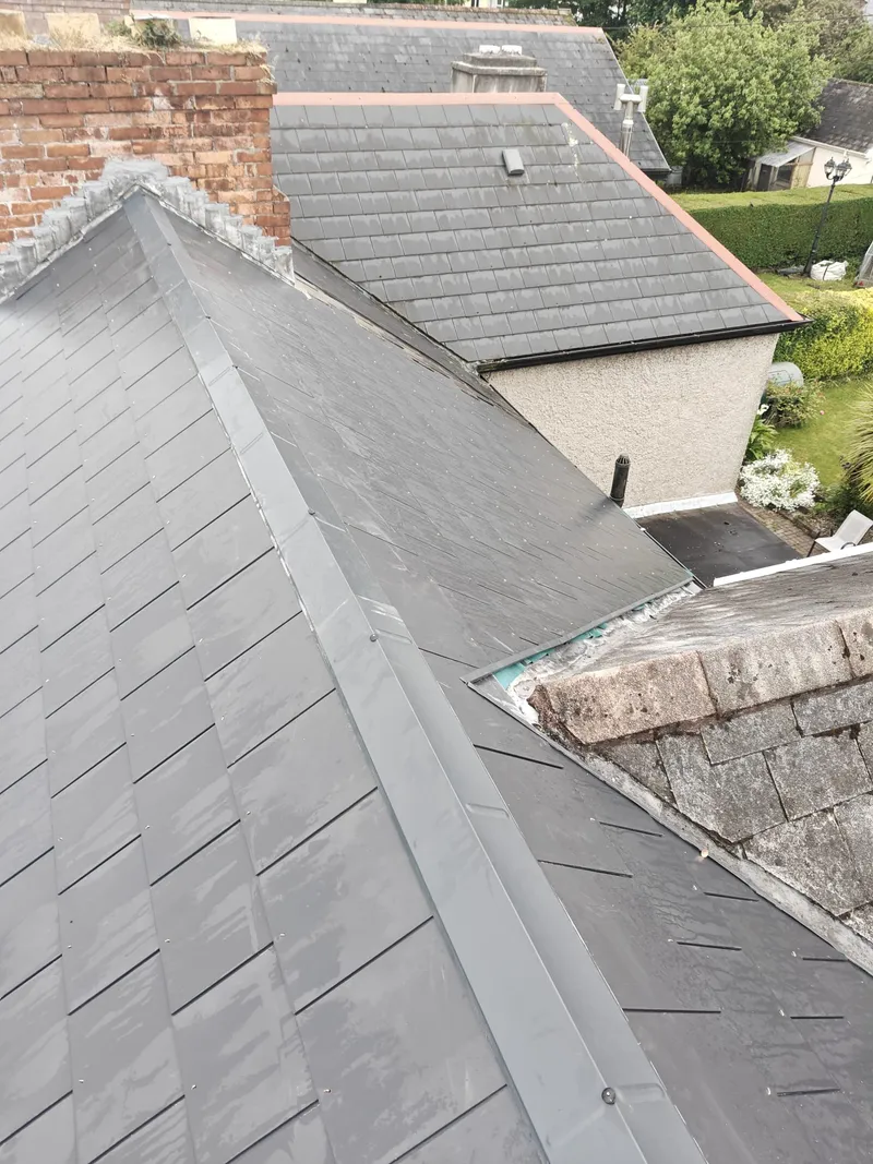 A slate roof with a lead-lined valley and ridge, and a stone chimney at the top of the slope